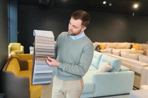 knap elegant jongen met baard zitten, Holding palet, op zoek, aanraken. concept van meubilair buying foto