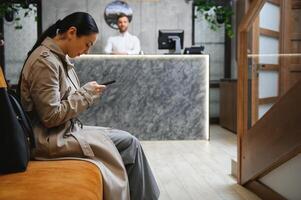 zakenvrouw met bagage in modern hotel lobby gebruik makend van smartphone foto