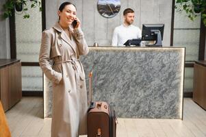elegant bedrijf vrouw met reizen trolley bagage in hotel lobby foto