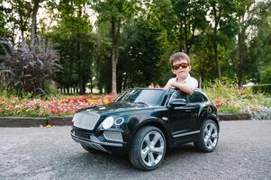 schattig jongen in rijden een zwart elektrisch auto in de park. grappig jongen ritten Aan een speelgoed- elektrisch auto. kopiëren ruimte. foto