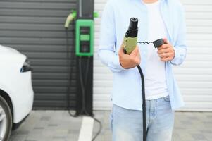 Mens Holding macht levering kabel Bij elektrisch voertuig opladen station. detailopname foto