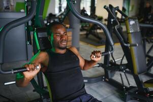 atletisch jong zwart Mens hebben training Aan borst druk op machine in Sportschool foto