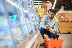 portret van gelukkig Indisch Mens staand in voorkant van de Product teller in een kruidenier op te slaan. Mens buying kruidenier voor huis in supermarkt. foto