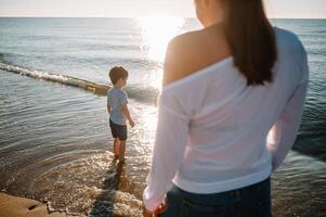 moeder en zoon spelen Aan de strand Bij de zonsondergang tijd. concept van vriendelijk familie. foto