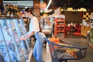 jong vrouw met een boodschappen doen zak net zo een klant buying vis Bij de gekoeld plank in de supermarkt foto