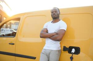 Afrikaanse Mens Holding in rekening brengen kabel in Aan hand- staand in de buurt luxe elektrisch auto foto