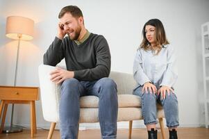 paar ruzie maken. vrouw geschreeuw naar haar ten einde raad man zittend Aan een bankstel in de leven kamer Bij huis foto