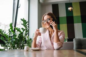 bedrijf vrouw Aan de telefoon Bij kantoor. jong bedrijf vrouw hebben telefoon telefoontje Bij de kantoor. glimlachen bedrijf vrouw. mooi jong bedrijf gebruik makend van smartphone Bij de zolder kantoor. foto