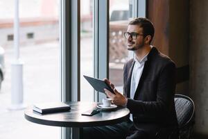 een Mens zittend in een cafe met tablet. gewoontjes Mens gebruik makend van tablet computer zittend in cafe surfing internet foto