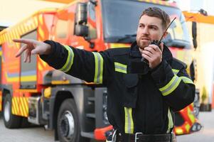 brandweerman in uniform gebruik makend van portable radio reeks in de buurt brand vrachtauto buitenshuis foto