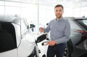 een gelukkig Mens kiest een nieuw elektrisch auto Bij een auto dealerschap. de concept van buying een ecologisch auto foto