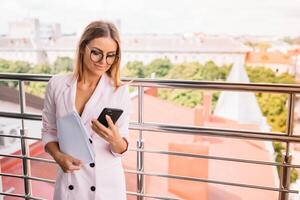 glimlachen zakenvrouw gekleed in formeel slijtage hebben aangenaam gesprek Aan mobiel telefoon met vriend, gelukkig aantrekkelijk vrouw sprekend Aan cel telefoon terwijl resting in kantoor interieur na werk. foto