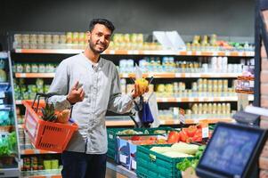 portret van gelukkig Indisch Mens staand in voorkant van de Product teller in een kruidenier op te slaan. Mens buying kruidenier voor huis in supermarkt. foto