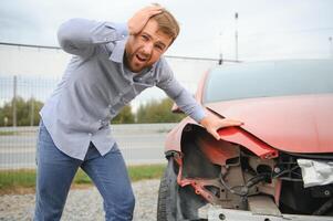 een gefrustreerd Mens in de buurt een gebroken auto. gepakt mijn hoofd realiseren de schade is echt, de auto is verder reparatie foto