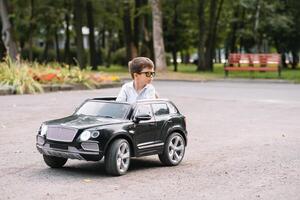 schattig jongen in rijden een zwart elektrisch auto in de park. grappig jongen ritten Aan een speelgoed- elektrisch auto. kopiëren ruimte. foto