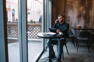 jong zakenman pratend Aan mobiel telefoon terwijl werken Aan tablet in cafe. foto