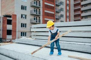 architect in helm schrijven iets in de buurt nieuw gebouw. weinig schattig jongen Aan de gebouw net zo een architect. foto