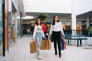 mooi jong mam en tiener- dochter zijn Holding boodschappen doen Tassen en glimlachen terwijl aan het doen boodschappen doen in winkelcentrum. familie boodschappen doen foto