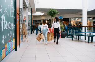 mooi jong mam en tiener- dochter zijn Holding boodschappen doen Tassen en glimlachen terwijl aan het doen boodschappen doen in winkelcentrum. familie boodschappen doen foto