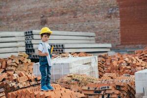 architect in helm schrijven iets in de buurt nieuw gebouw. weinig schattig jongen Aan de gebouw net zo een architect foto