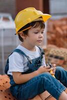 architect in helm schrijven iets in de buurt nieuw gebouw. weinig schattig jongen Aan de gebouw net zo een architect foto