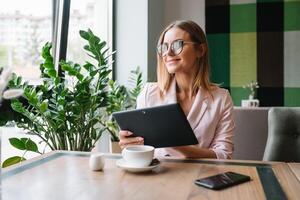 jong glimlachen zakenvrouw drinken koffie en gebruik makend van tablet computer in een koffie winkel foto