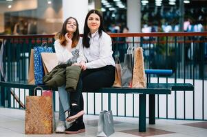 mooi jong mam en tiener- dochter zijn Holding boodschappen doen Tassen en glimlachen terwijl aan het doen boodschappen doen in winkelcentrum. familie boodschappen doen foto