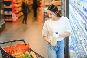 glimlachen gelukkig vrouw genieten van boodschappen doen Bij de supermarkt, ze is leunend Aan een vol kar foto