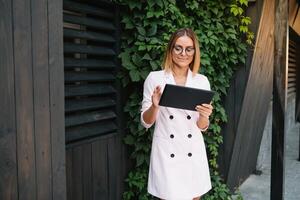 portret van een geslaagd zakenvrouw Holding een digitaal tablet stootkussen en een map terwijl trots staand in de buurt kantoor. foto