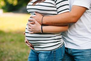 beeld van zwanger paar. man aanraken zijn vrouw buik met handen. zwanger vrouw buitenshuis. foto