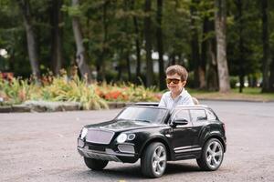 schattig jongen in rijden een zwart elektrisch auto in de park. grappig jongen ritten Aan een speelgoed- elektrisch auto. kopiëren ruimte. foto