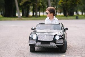 schattig jongen in rijden een zwart elektrisch auto in de park. grappig jongen ritten Aan een speelgoed- elektrisch auto. kopiëren ruimte. foto