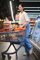 boodschappen winkelen. portret van glimlachen gelukkig vrouw leunend Aan trolley kar in supermarkt foto