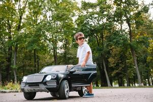 schattig jongen in rijden een zwart elektrisch auto in de park. grappig jongen ritten Aan een speelgoed- elektrisch auto. kopiëren ruimte. foto