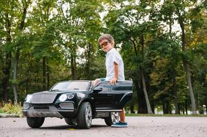 schattig jongen in rijden een zwart elektrisch auto in de park. grappig jongen ritten Aan een speelgoed- elektrisch auto. kopiëren ruimte. foto