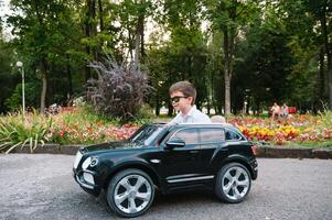 schattig jongen in rijden een zwart elektrisch auto in de park. grappig jongen ritten Aan een speelgoed- elektrisch auto. kopiëren ruimte. foto