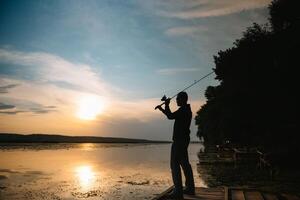 visser Bij zonsondergang Aan de rivier- .mooi zomer landschap met zonsondergang Aan de rivier. vissen. spinnen Bij zonsondergang. silhouet van een visser. foto