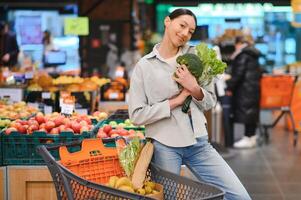 jong vrouw kiest broccoli, buying groenten in supermarkt. foto