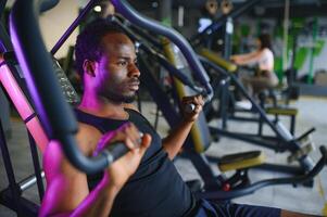 atletisch jong zwart Mens hebben training Aan borst druk op machine in Sportschool foto