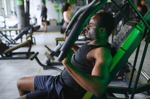 atletisch jong zwart Mens hebben training Aan borst druk op machine in Sportschool foto