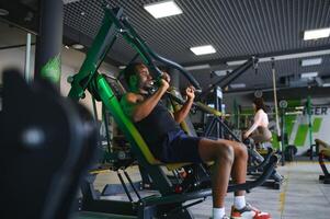 atletisch jong zwart Mens hebben training Aan borst druk op machine in Sportschool foto