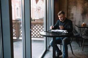 knap zakenman gebruik makend van een digitaal tablet en drinken koffie terwijl zittend in cafe in de stad centrum. foto