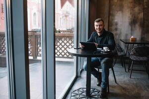 knap zakenman gebruik makend van een digitaal tablet en drinken koffie terwijl zittend in cafe in de stad centrum. foto