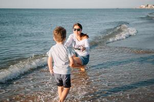 moeder en zoon spelen Aan de strand Bij de zonsondergang tijd. concept van vriendelijk familie. foto