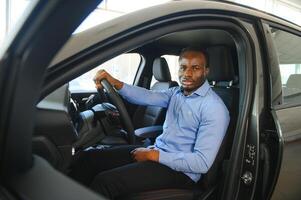 auto baasje. blij afro vent lachend, zittend in nieuw auto- het rijden van handel winkel foto