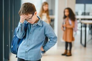 van streek jongen Bij school- aan het bedekken zijn gezicht met zijn handen. pesten Bij school- foto