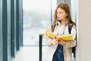 portret van glimlachen schoolmeisje staand met notitieboekje in gang Bij school- foto