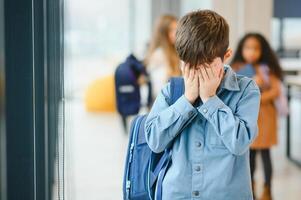 van streek jongen Bij school- aan het bedekken zijn gezicht met zijn handen. pesten Bij school- foto