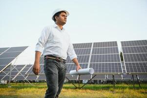 portret van jong Indisch mannetje ingenieur staand in de buurt zonne- panelen, met Doorzichtig blauw lucht achtergrond, hernieuwbaar en schoon energie. vaardigheid Indië, kopiëren ruimte foto