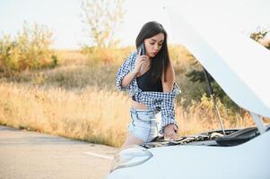 jong sexy vrouw met gebroken auto roeping Aan de cel telefoon. foto